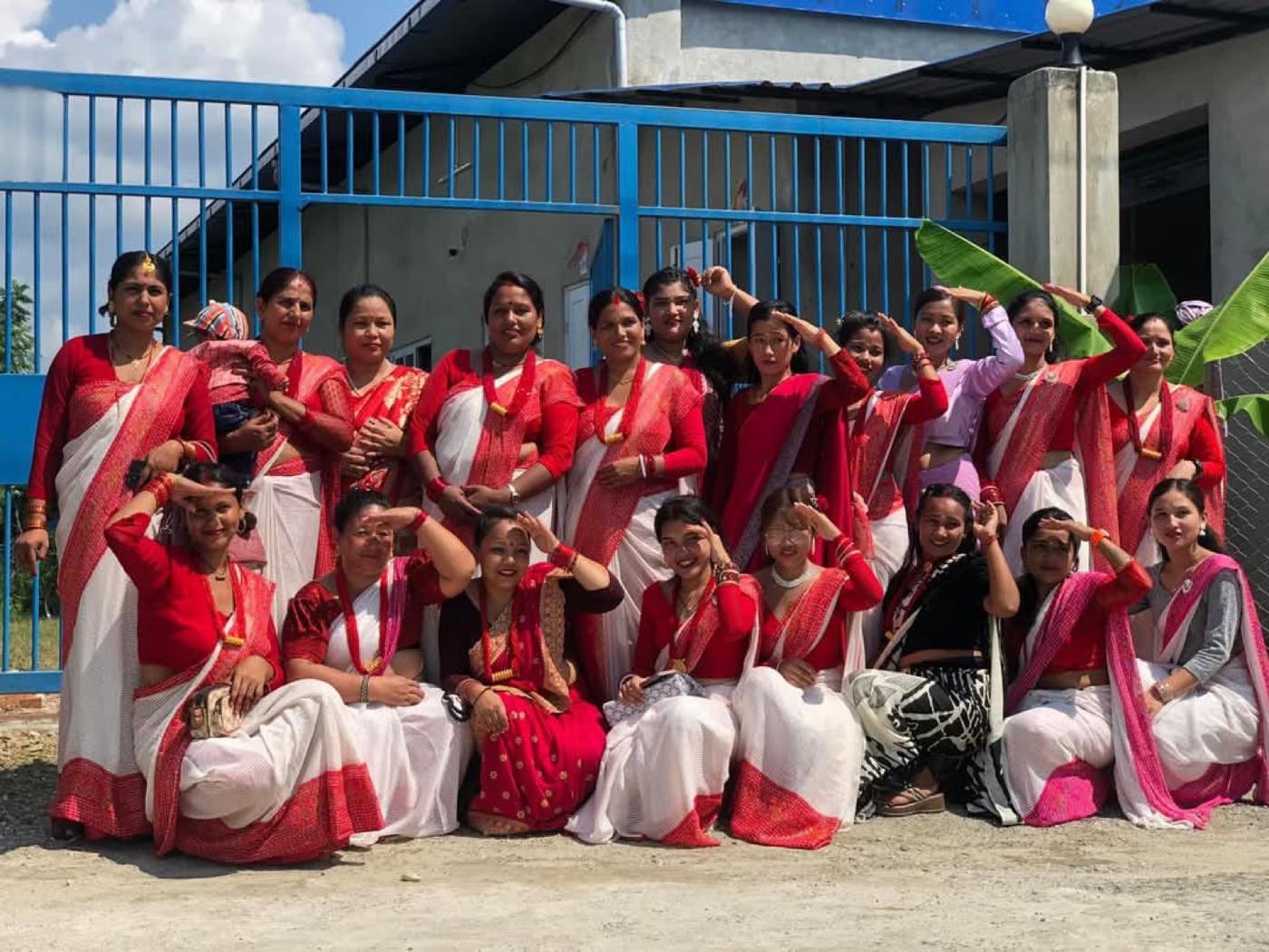Women of the Trishakti Apparel team in red and white saris outside the factory gate in Gaindakot, Nepal, celebrating Teej