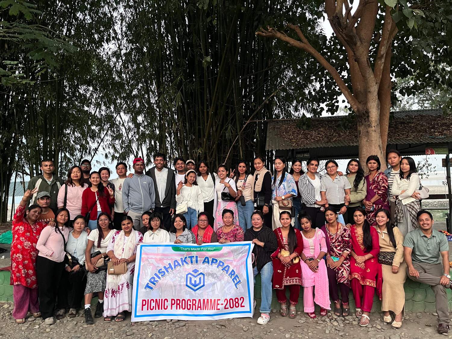 The full Trishakti Apparel workforce at the 2082 company picnic, holding the Trishakti Apparel banner